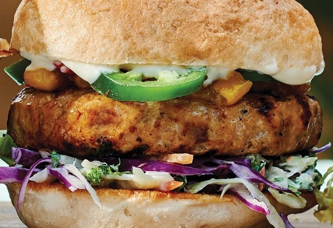 Gros plan d’un burger gourmet de poulet préparé à partir de surgelés avec diverses garnitures dans un pain