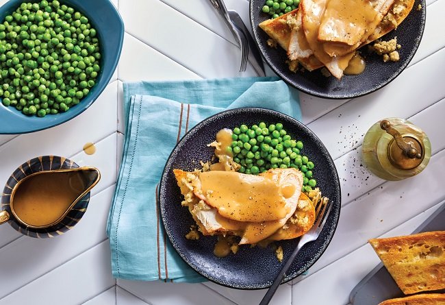 Deux assiettes de dinde avec sauce, accompagnements et légumes verts sur une table blanche