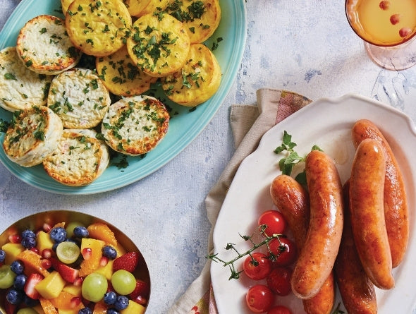 Assortiment de plats brunch incluant saucisses, salade de fruits et bouchées d’omelette sur une table