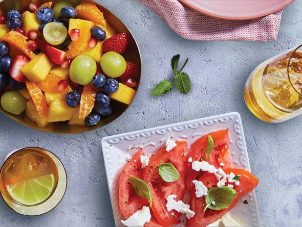 Salade de fruits dans un bol et tomates avec fromage feta sur une surface bleu pâle