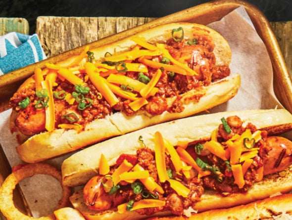 Deux hot-dogs garnis de chili, fromage et oignons verts dans des pains, servis sur un plateau en bois