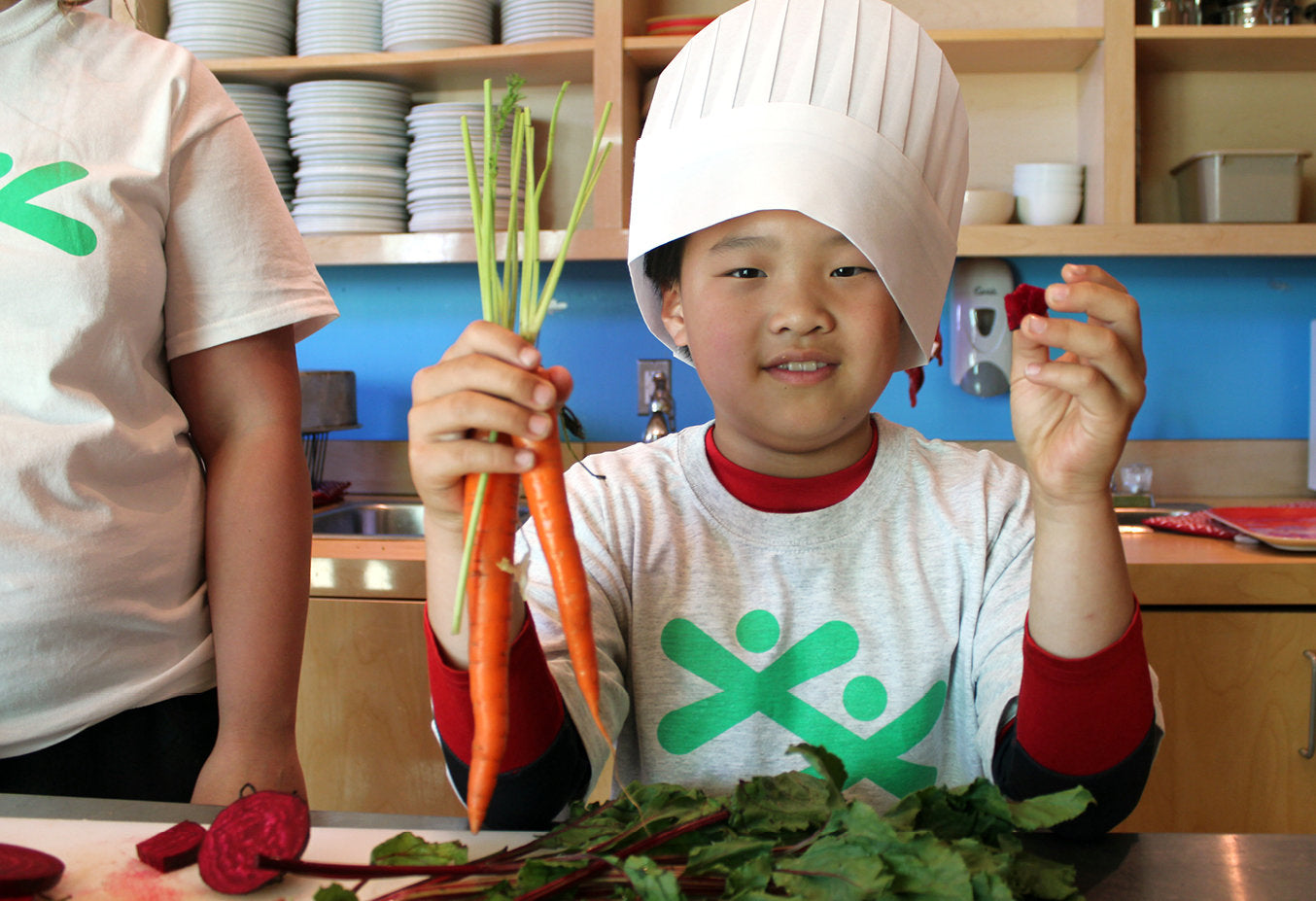 Enfant tenant des carottes et des radis dans une cuisine