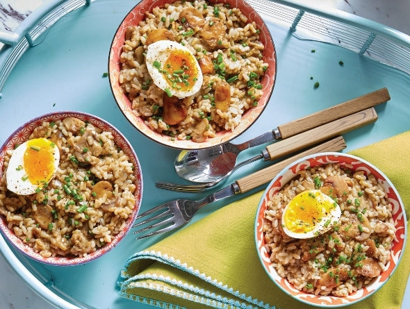 Trois bols de risotto aux champignons avec œufs et légumes sur un plateau bleu avec ustensiles