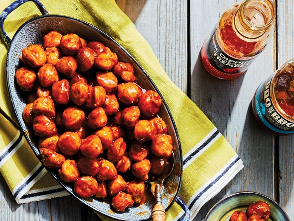 Boulettes surgelées cuites au four dans un plat de cuisson avec une bouteille de sauce piquante sur une table en bois