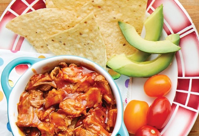 Bol de porc effiloché avec croustilles de tortilla, avocat et tomates cerises sur une assiette colorée